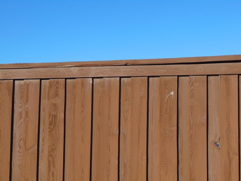 Close-up view of a wooden privacy fence against a blue sky