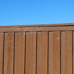 Close-up view of a wooden privacy fence against a blue sky