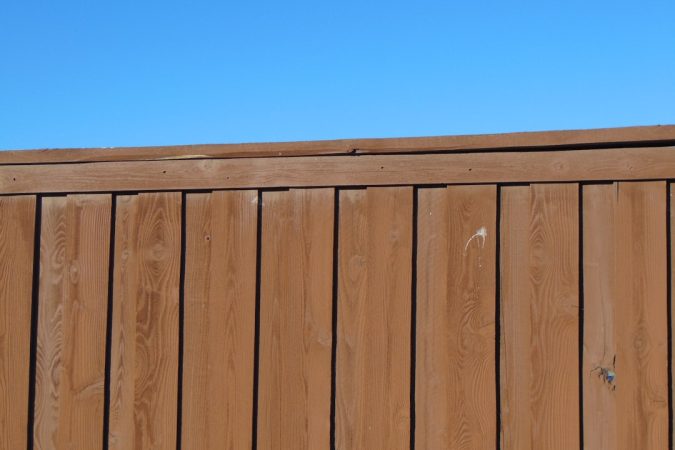 Close-up view of a wooden privacy fence against a blue sky