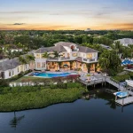 Aerial view of a waterfront home in Jupiter, FL, surrounded by lush greenery and palm trees at sunset.