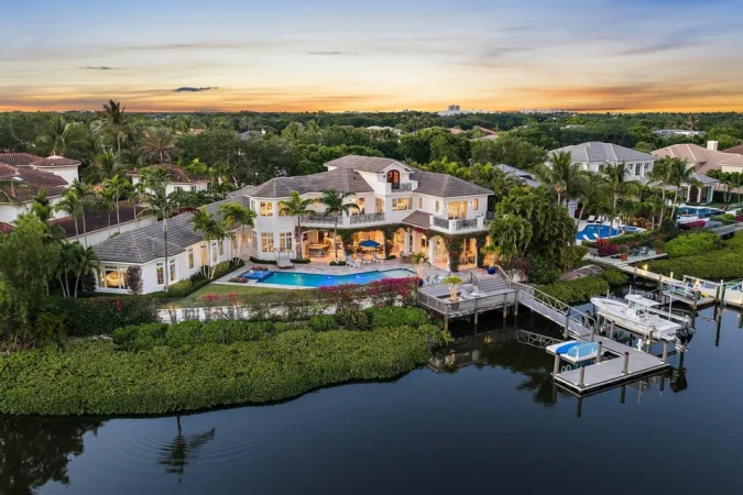 Aerial view of a waterfront home in Jupiter, FL, surrounded by lush greenery and palm trees at sunset.