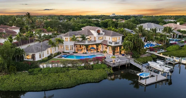 Aerial view of a waterfront home in Jupiter, FL, surrounded by lush greenery and palm trees at sunset.